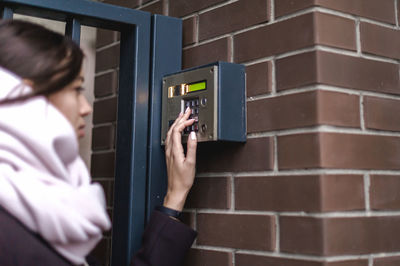 Woman typing push buttons of biometrics machine on wall