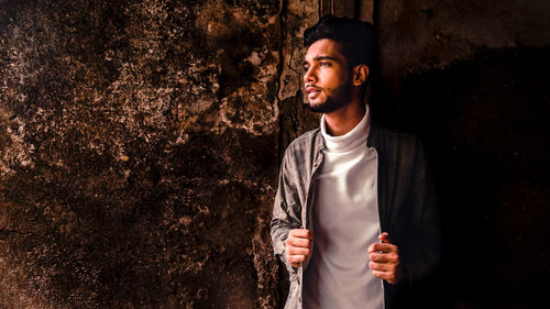 Young man looking away while standing against wall