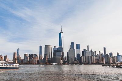 Modern buildings by river in city against sky