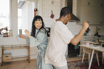 Joyful female and male friend dancing at home