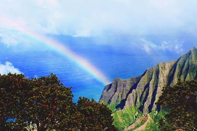 Scenic view of rainbow over trees against sky and cliff