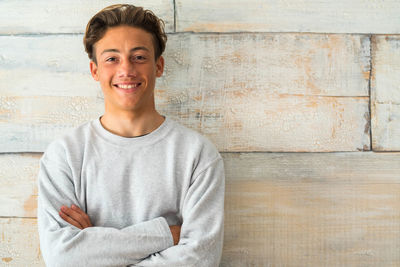 Portrait of smiling teenage boy with arms crossed standing against wall