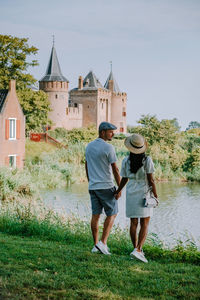 Rear view of couple holding hands standing by lake against church