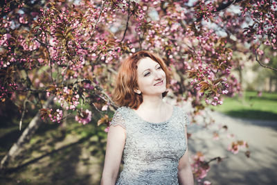 Happy middle aged armenian woman in an elegant dress under the blooming sakura tree. smiling