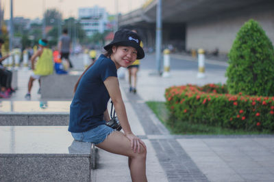Portrait of smiling young woman wearing hat sitting on seat in city