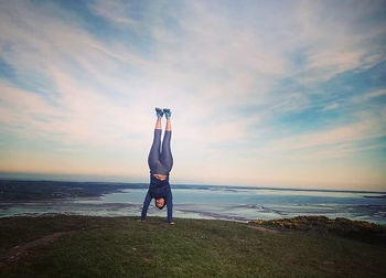 Rear view of man standing on beach against sky during sunset