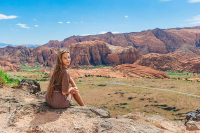 Side view of woman sitting on rock against sky