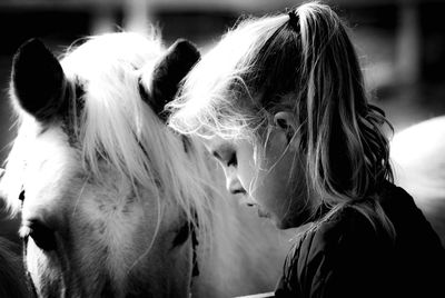 Side view of girl standing by horse at barn