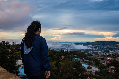 Young girl watching downtown city view with dramatic cloudy sky at evening from mountain top