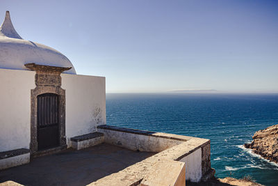 Building by sea against clear blue sky