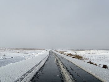 Empty road amidst snow covered landscape against sky