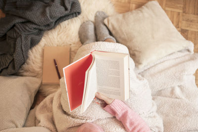 Low section of woman reading book on bed at home