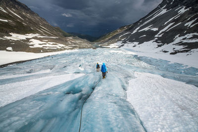 Rear view of people hiking on glacier by snowcapped mountains against sky