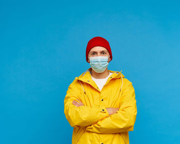 Waisted portrait of man in protective medical mask stands with his arms crossed