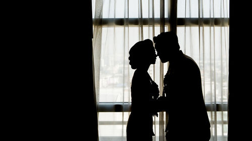 Silhouette man and woman standing against window