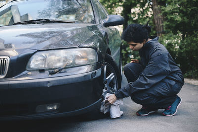 Full length of female mechanic cleaning car wheel outside auto repair shop