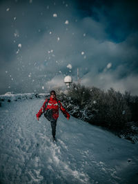 Person walking on snow covered field against sky