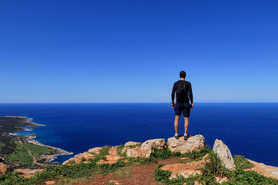 Rear view of man looking at sea against blue sky