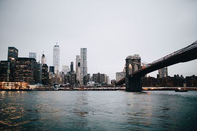 Brooklyn bridge over east river by cityscape against clear sky