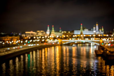 Illuminated city by river against sky at night