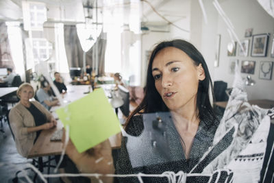 Businesswoman writing on sticky note while explaining colleagues during meeting in creative office