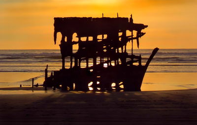 Silhouette pier on beach against sky during sunset