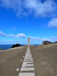 Walkway leading towards sea against blue sky