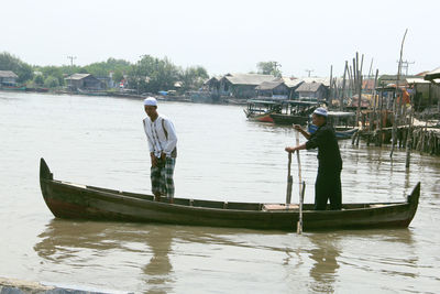Men standing on boat in river against sky