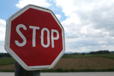 Close-up of stop sign by field against sky