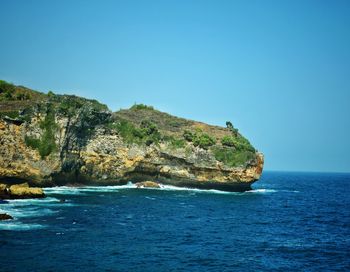 Scenic view of cliff by sea against clear blue sky