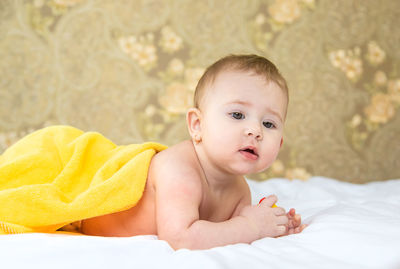 Baby girl under yellow towel lying on bed at home