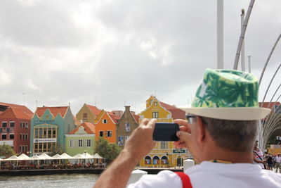 Rear view of man photographing river and buildings with smart phone
