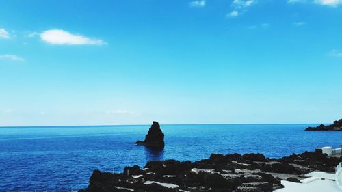 Scenic view of rocks by sea against blue sky