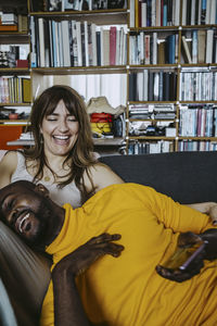 Cheerful man leaning on girlfriend laughing sitting on sofa in living room at home