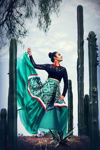 Low angle view of beautiful woman looking away while standing by cactus against sky