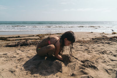 Full length of man sitting on shore at beach against sky