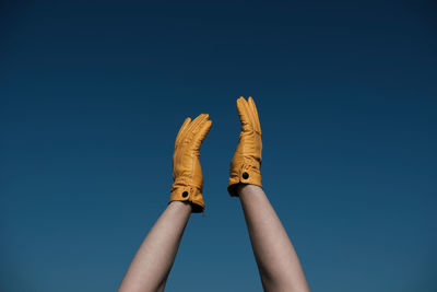 Cropped hands wearing yellow gloves against clear blue sky