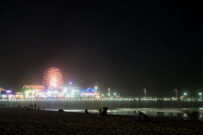 Illuminated ferris wheel by santa monica pier at night