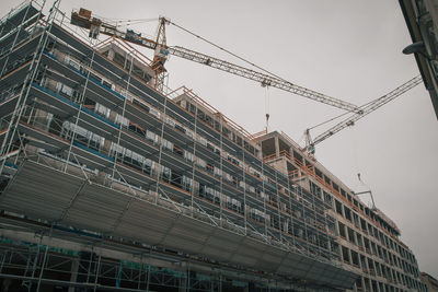 Low angle view of crane by building against sky