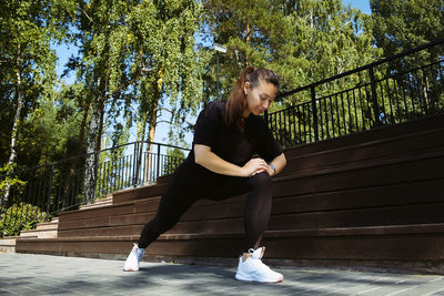 Girl in sportswear on a sunny summer day on the embankment in the park doing fitness and stretching