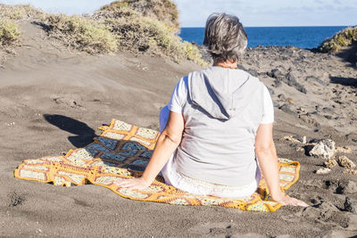 Rear view of woman sitting at beach during sunny day