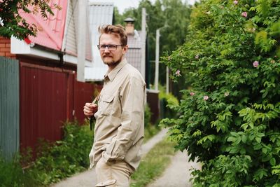 Portrait of man standing by plants against houses