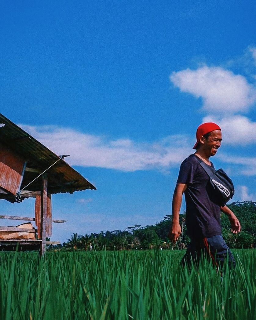 sky, field, architecture, land, grass, built structure, plant, building exterior, nature, three quarter length, real people, men, day, standing, landscape, cloud - sky, agriculture, growth, blue, lifestyles, outdoors