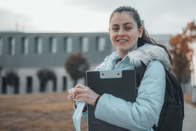 Portrait of young woman holding clipboard outdoors