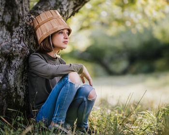 Portrait of young woman wearing hat sitting on land