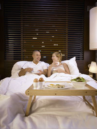 Smiling couple having coffee while relaxing on bed in hotel room