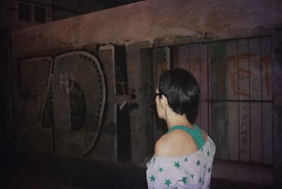 Woman standing by graffiti on wall at night