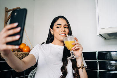 Portrait of young woman taking selfie while drinking juice