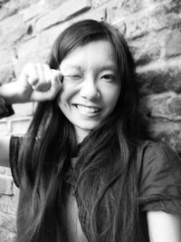 Close-up portrait of woman making face while clenching fist by brick wall