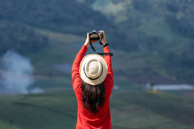 Asian female tourist wearing a bright red shirt taking pictures of beautiful natural scenery.